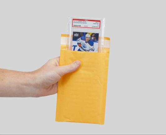 Hand holding yellow envelope with trading card, perfect for shipping trading cards safely.